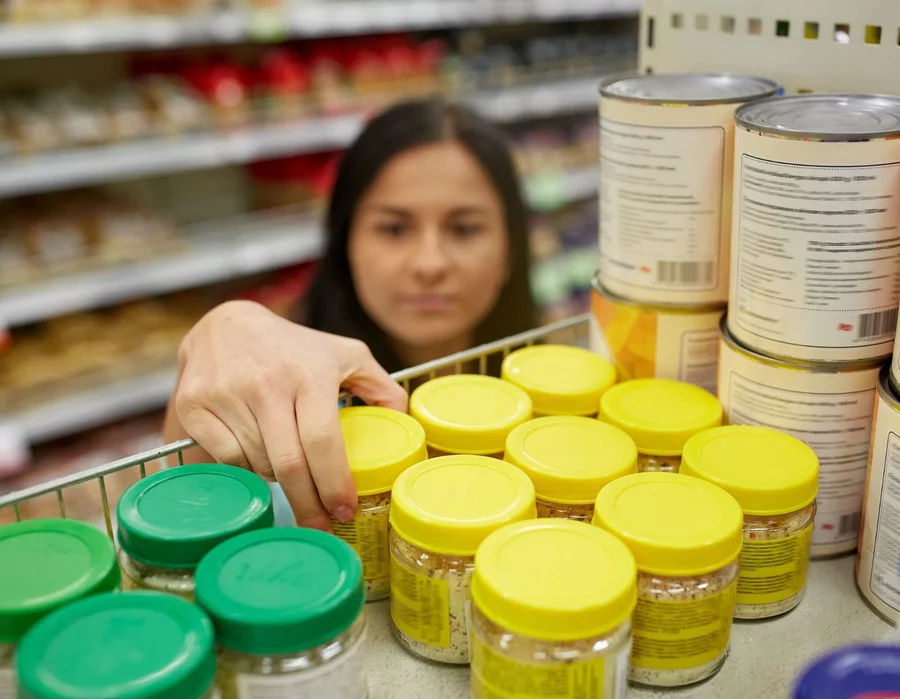 woman taking jar with food from shelf at grocery